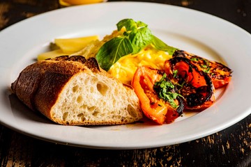 Breakfast plate with scrambled eggs, cheddar cheese, fresh basil, grilled tomatoes and crispy baguette. Classic traditional American Restaurant breakfast or brunch favorite. 