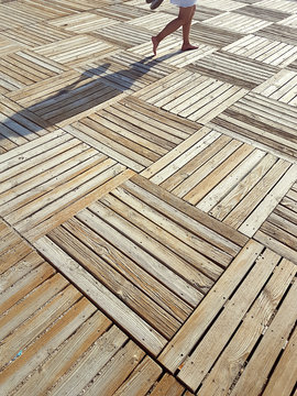 Vacation, travel, carefree concept. Female legs on geometric pattern wooden parquet on beach in sunny day.