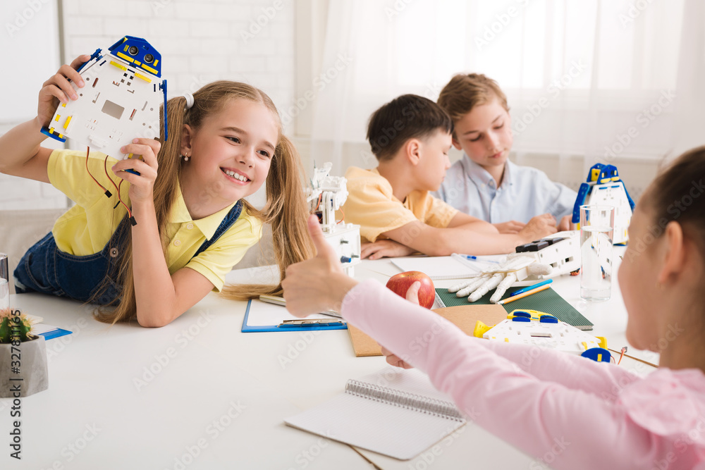 Poster girl showing robot to friend and classmate showing thumb up