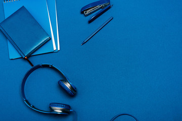 top view of notebooks, headphones, pen, stapler on blue background