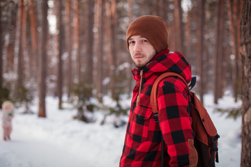 Male tourist with backpack walks on snow pine forest. Guy hiking at nature. Concept of winter holiday or vacation..