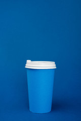paper cup with coffee on blue background with copy space