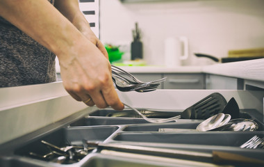 The woman is taking the kitchen equipment  from the shelf with kitchenware