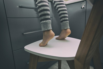 Child climbs on stool, trying to reach things on the kitchen's table