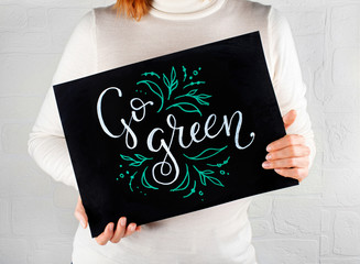 Woman keeping a small chalkboard with GO GREEN lettering