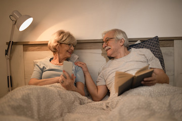 Happy mature couple talking while lying in bedroom in the evening.