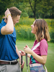 Happy golfer couple hugging and talking together at green field outdoor.