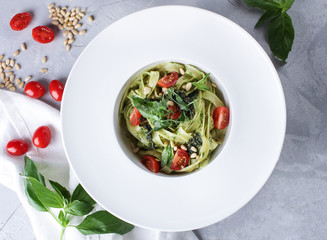 The concept of Italian cuisine. Pasta with pesto sauce and pine nuts, fresh herbs and cherry tomatoes in a white deep dish. Background image, copy space