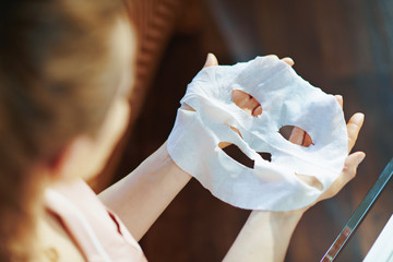 middle age housewife holding white sheet facial mask