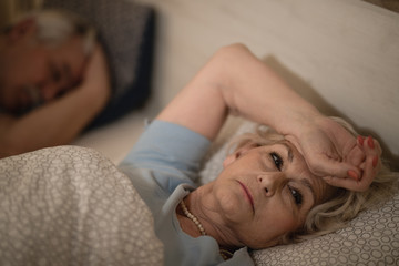 Worried mature woman lying in bed and thinking of something.