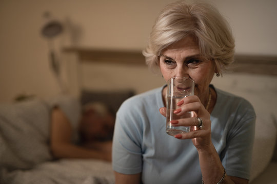 Pensive Senior Woman Drinking Water At Night In Bedroom.