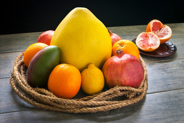 Fruits are tied with a decorative palm rope and lie on a gray rustic tabletop against a dark wall.
