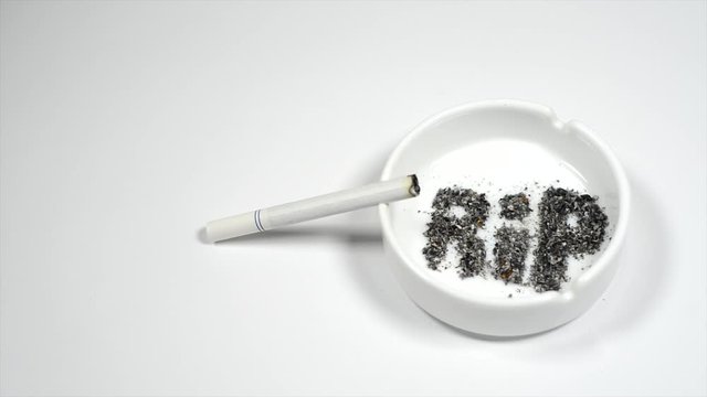 Image with word RIP transform into skull from ash inside ashtray on white. Smoldering cigarette on ashtray.