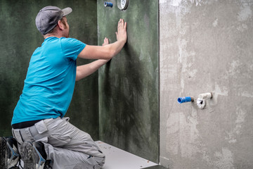 Handwerker montiert XXL Fliese an die Wand in der Dusche