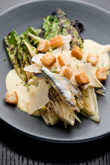 Caesar Salad. Grilled Romaine lettuce leaves topped with classic Caesar salad dressing and garnished with butter garlic croutons shaved parmesan cheese and whole anchovies. Classic American Salad.