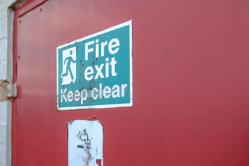 Shallow focus of an old Fire Exit and No Smoking sign seen attached for a fire door, used for emergency exit for a warehouse and logistics company.