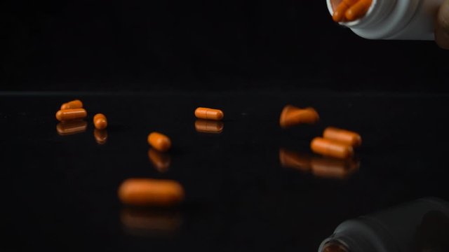 Slow motion shot of orange pills falling on the mirrored black table and bounced. Drugs, medicine addiction concept