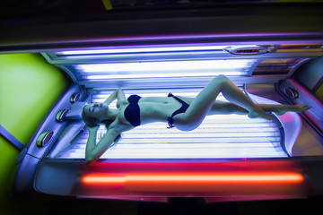 Beautiful young woman lying in solarium and sunbathing