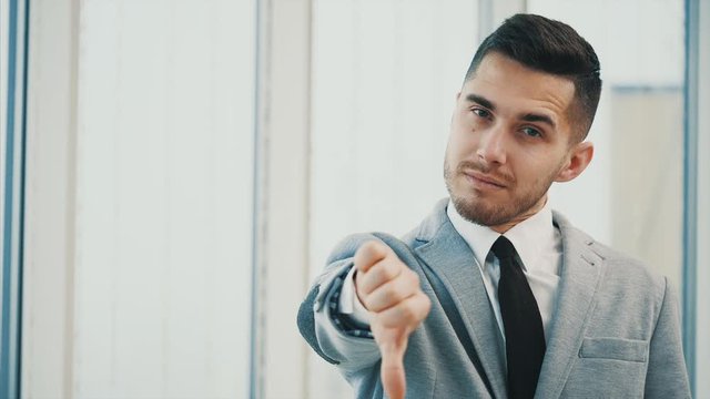Business man is looking seriously for camera with his thumb finger up, then he turns it dowm, isolated on white panoramic background. Close up. Copy space. 4K.