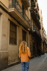 Fototapeta na wymiar Girl walking through the streets in Barcelona. Cute girl with blond curly hair walking through the streets on Barcelona looking at the buildings and doing tourism