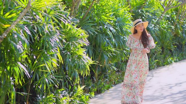 Girl walks beside palm bushes wearing flowery vacation dress and hat