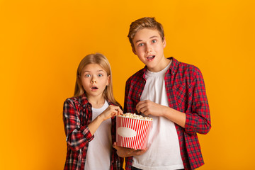 Shocked siblings eating popcorn and opening mouth in amazement