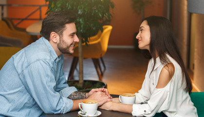Boyfriend And Girlfriend Holding Hands Flirting In Cafe, Side View