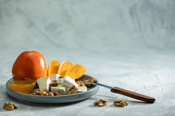 Brie cheese and persimmon with almonds and walnuts on a plate and a grey background. Space for text