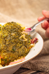 Vegetable salad in a white ceramic bowl on a background of rough homespun fabric. Someone is stirring the salad with a fork. Close up.