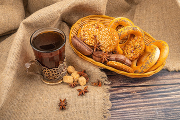 Cookies, chocolate cakes, bagels, star anise in a wicker basket and a glass of tea in a vintage Cup holder against a background of rough homespun fabric. Close up.