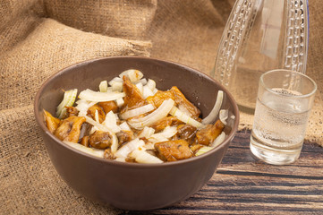 Salted mushrooms with onions in a ceramic bowl, a glass of vodka and a decanter on a background of rough homespun fabric. Country food. Close up.