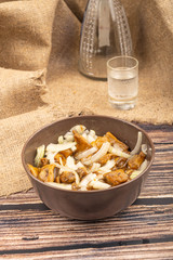 Salted mushrooms with onions in a ceramic bowl, a glass of vodka and a decanter on a background of rough homespun fabric. Country food. Close up.