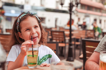 Little girl in a cafe on the street drinks juice. baby having fun and smiling
