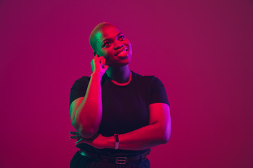 Thoughtful, dreaming. African-american young woman's portrait on purple background. Beautiful model in black shirt. Concept of emotions, facial expression, sales, ad, inclusion, diversity. Copyspace.