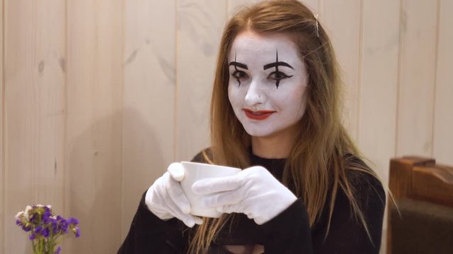 Funny female mime drink coffee in the cafe