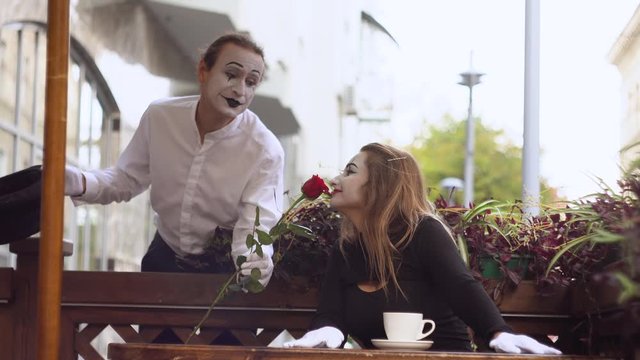 Two happy mime on a date in the cafe. Happy man giving a flower to his girlfriend