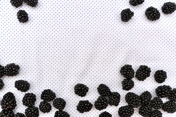 Background with a frame of fresh blackberry berries on a white background in fine polka dots.