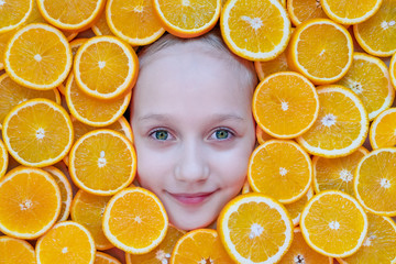 Portrait of a beautiful teenager girl with green eyes among sliced oranges. Orange frame. Healthy food concept and summer time