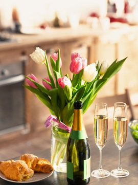 Bouquet of spring tulips, champagne and croissants on table in kitchen