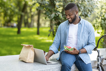 Happy afro businessman using laptop and having healthy lunch outdoors