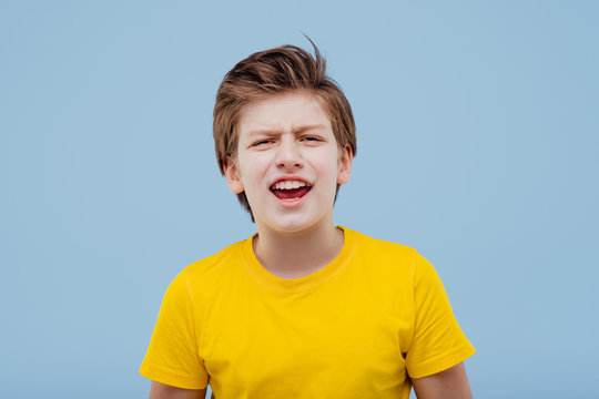 screaming young boy looks at camera in yellow t-shirt isolated on yellow background, copy space