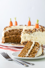 A close up of a carrot cake with cream cheese frosting and a slice of cake in front ready for eating.