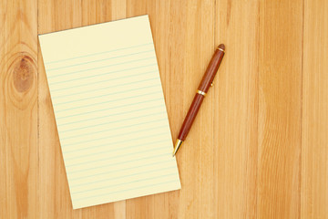 Yellow legal lined notepad paper with a pen on pine wood desk