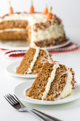 Close up of two pieces of carrot cake with cream cheese frosting and a cake in soft focus in the background.