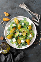 Avocado salad with yellow tomato, feta cheese, arugula and sunflower seeds. Top view with copy space. Healthy food.