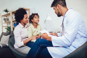 African American male pediatrician with stethoscope talking to little girl sitting on mother lap. - Powered by Adobe