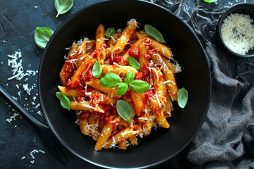 Penne pasta with tomato sauce, parmesan cheese and basil on dark background. Top view with copy space.