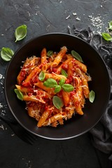 Penne pasta with tomato sauce, parmesan cheese and basil on dark background. Top view with copy space.