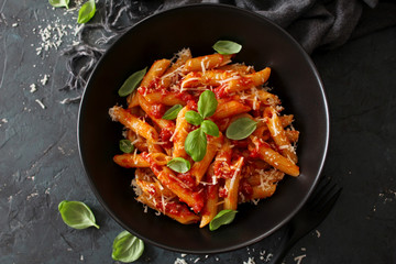 Penne pasta with tomato sauce, parmesan cheese and basil on dark background. Top view with copy...