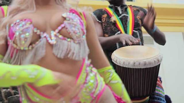 Beautiful girl bright colorful carnival costume decorated with rhinestones dancing samba. African drummers in ethnic clothes playing on djembe drum close up. Musician beats rhythm on african drums